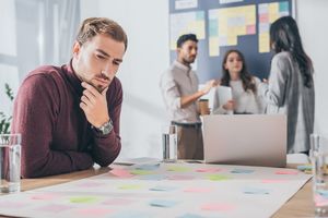 Scrum Master looking confused with reluctant team in stand-up meeting, all are upset, some members looking at the floor