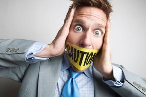 Businessman gagged with yellow caution tape holding his head in his hand