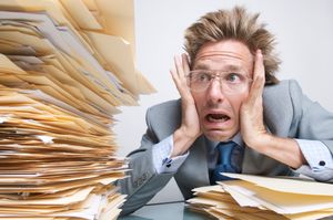 Stressed product manager looking with shock at a massive stack of file folders on his desk